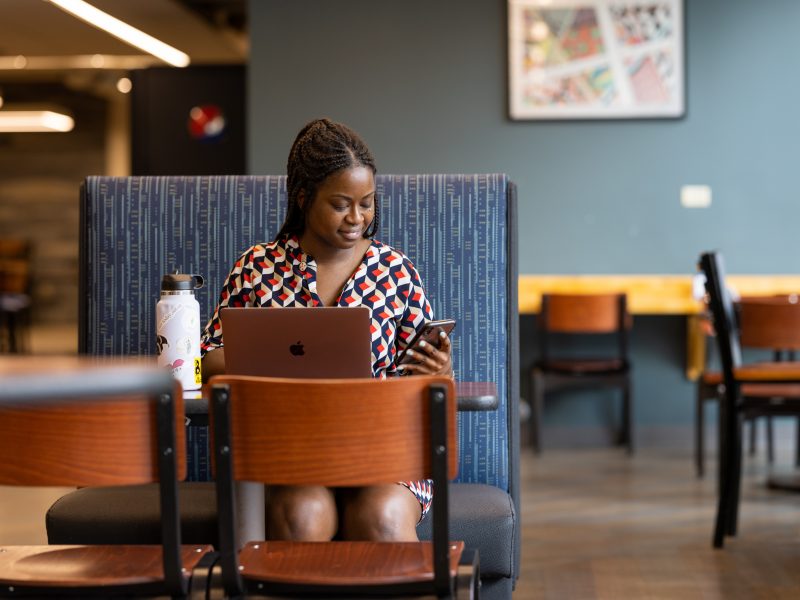 A photo a student sitting at a booth and working on a laptop.