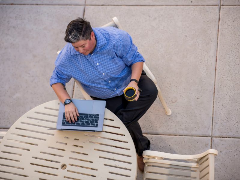 A photo of a person sitting and working on a computer with a cup of coffee.