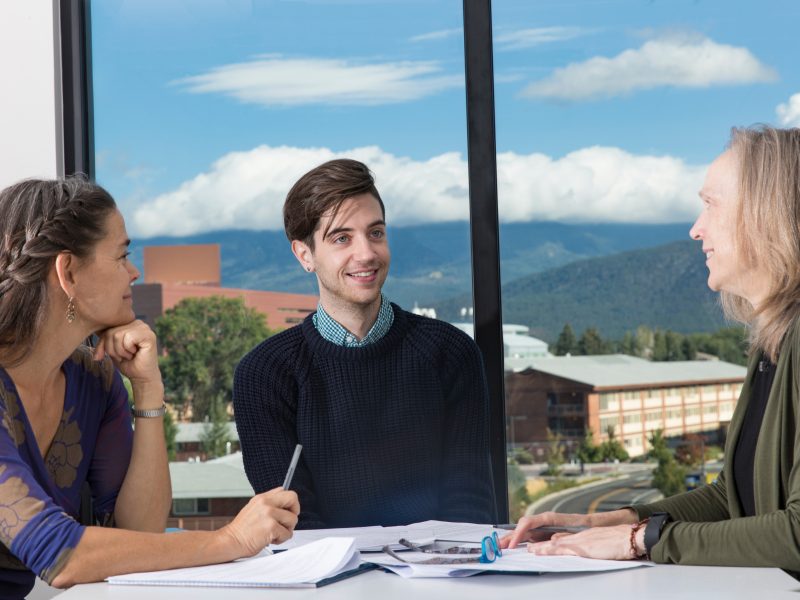 A photo of three people at a table speaking.