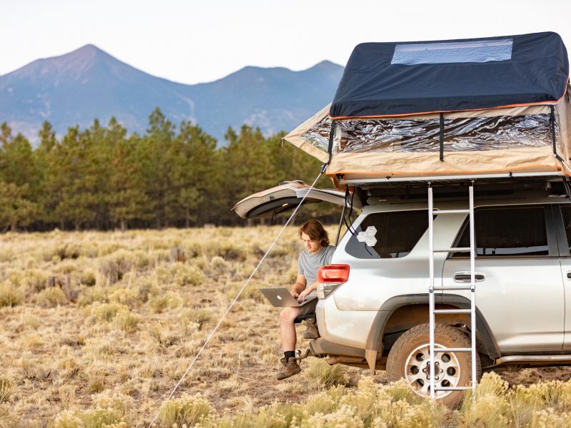 A photo of student working on a laptop outdoors in the trunk of a car.