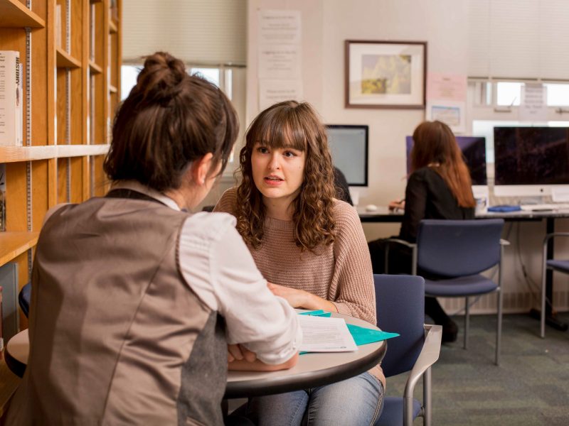 A photo of two students sitting at table and talking.