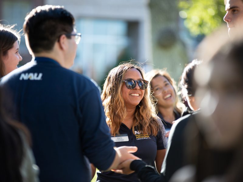 An orientation coordinator stands with students outside at orientation.