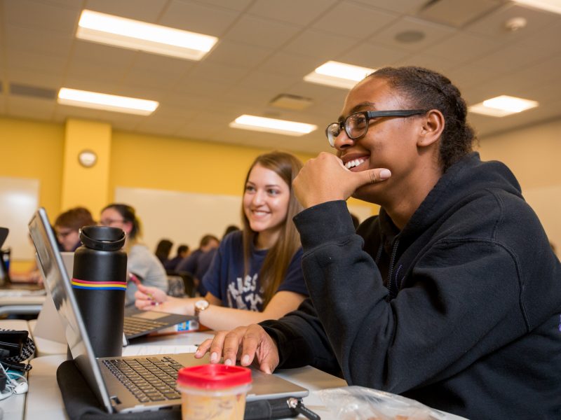 A candid photo of students smiling and working on their laptops.