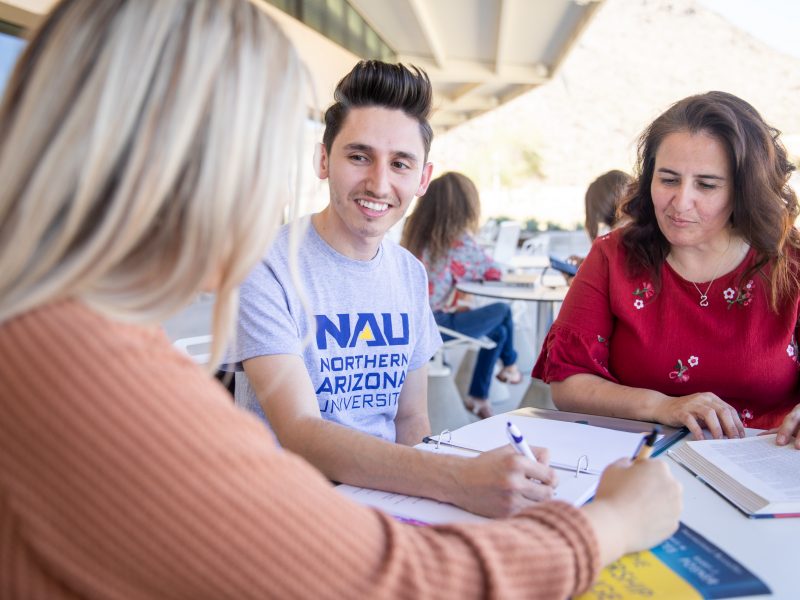 Student and parent discussing something with a faculty member around a table.