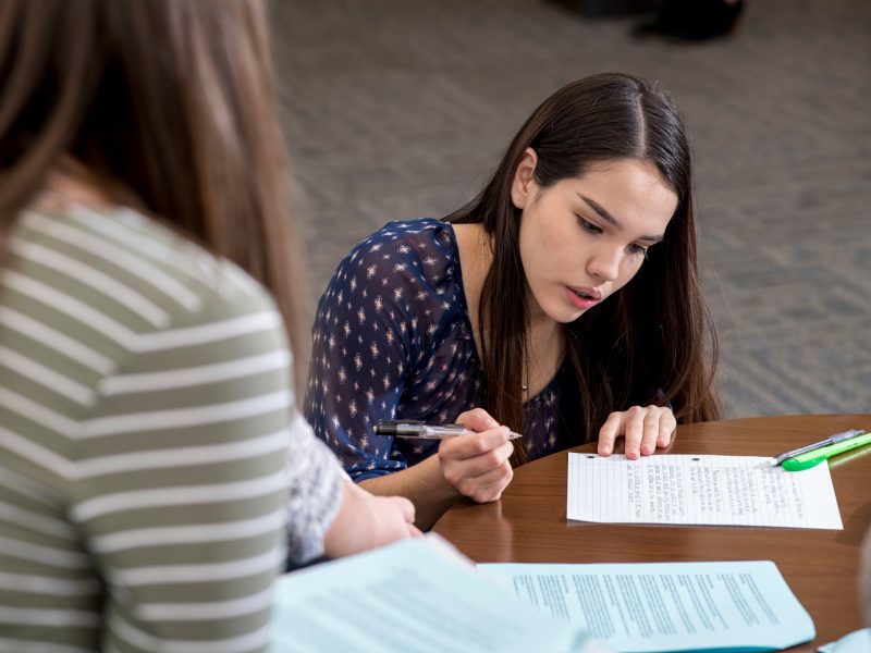 Students write on notebook paper at a table.
