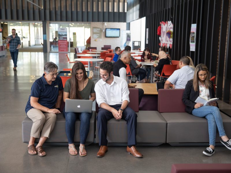 Students sitting in a common area overlooking one persons laptop.