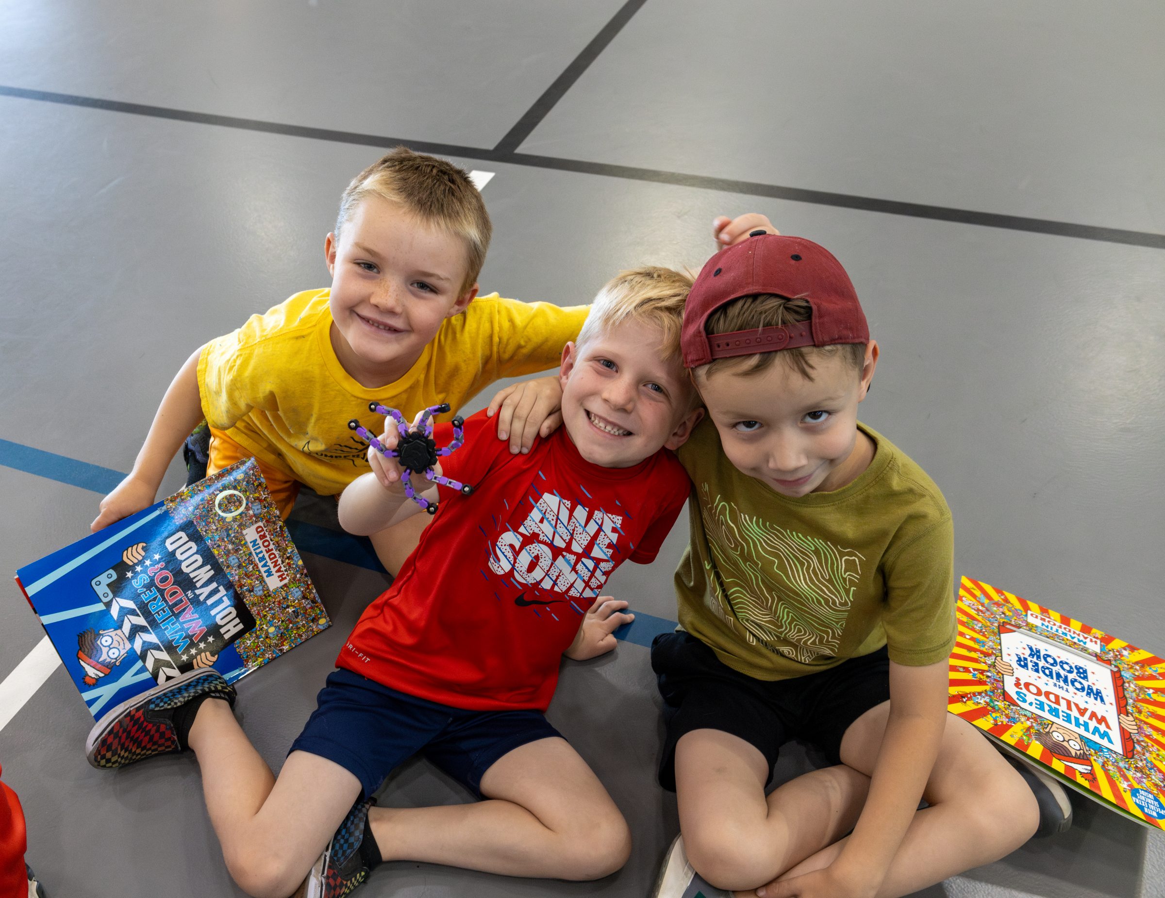 Three children smiling at the camera, reading a book