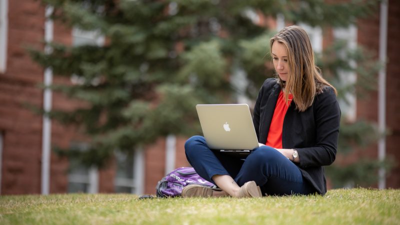 Student sitting on grass with a laptop.