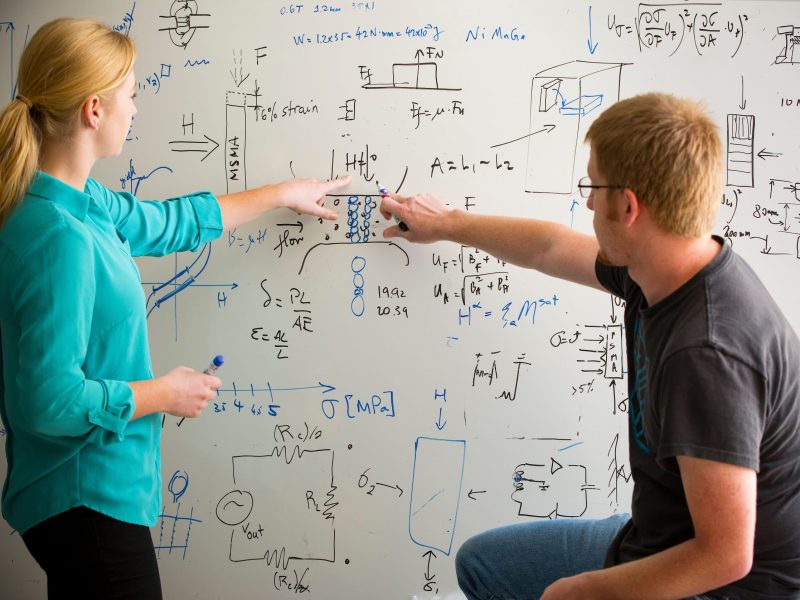 Two students working together on a engineering problem at a white board.