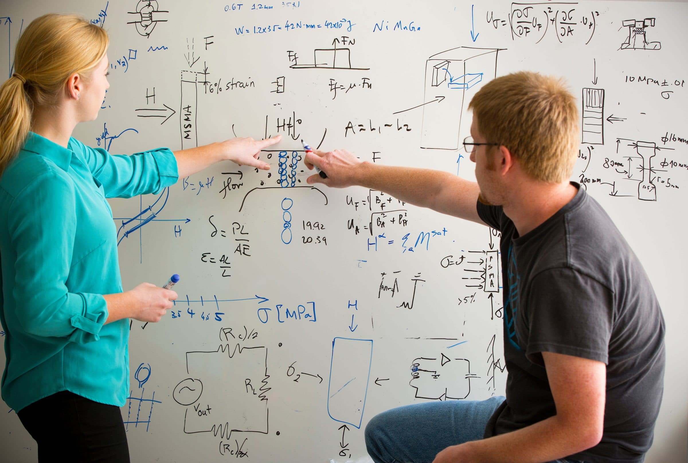 Two students working together on a engineering problem at a white board.