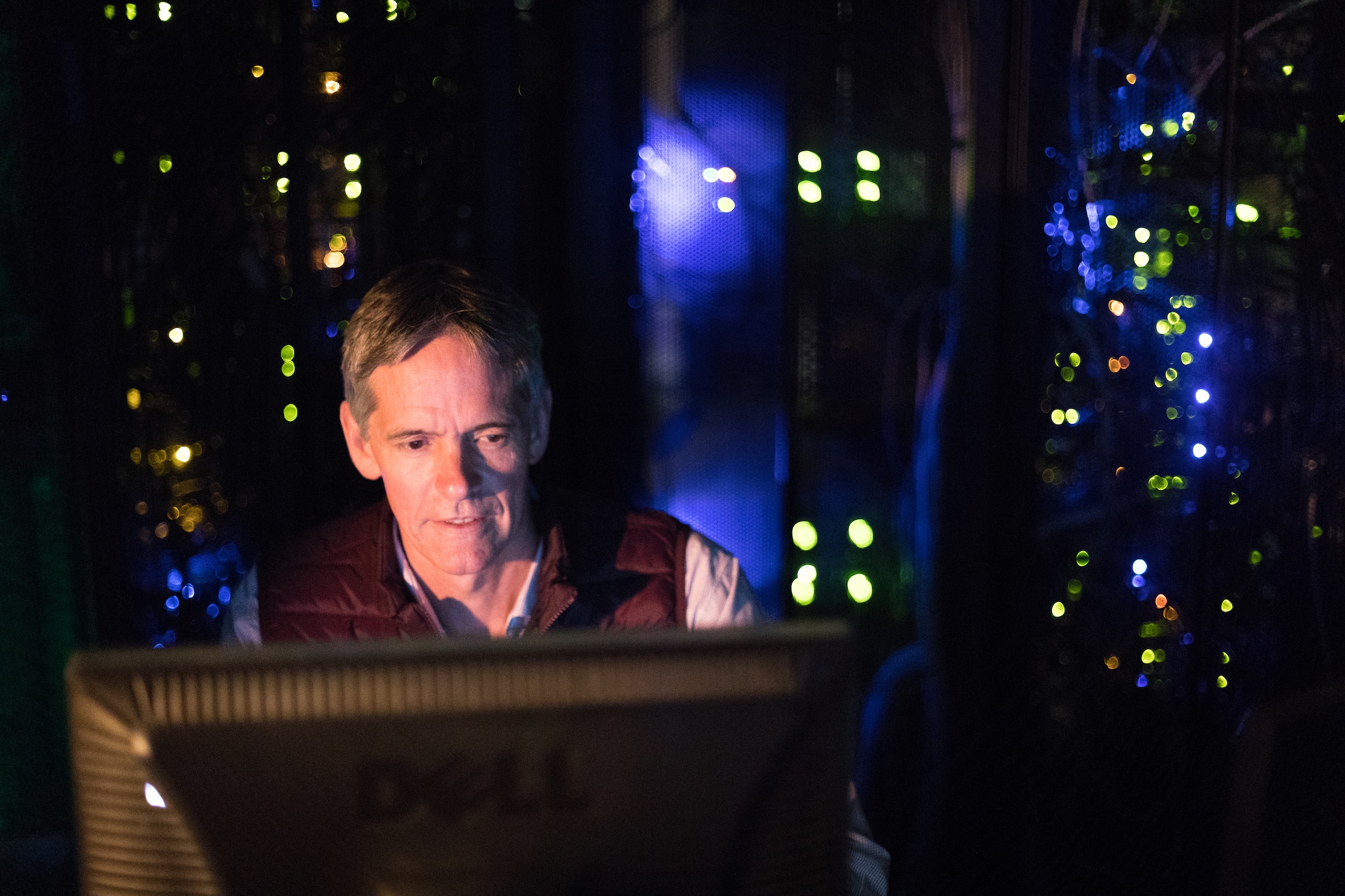 Scott Goetz sits in front of a computer in a dark room with lights..