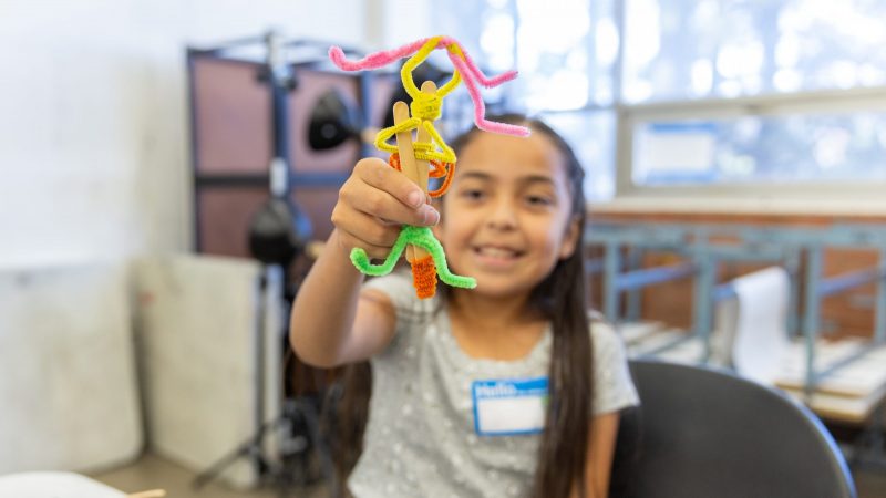 A child holds up a pipe cleaner creation in an early childhood learning setting
