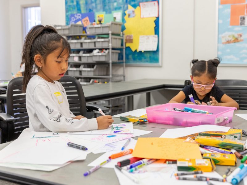 Two young children practice coloring at a school table