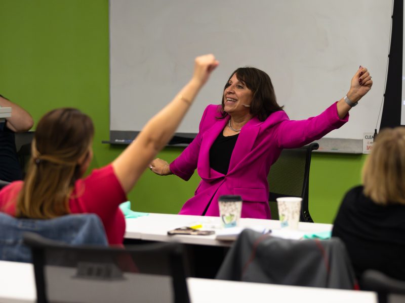 Bernadette Melynk speaking at RC event, raising her hand in a fist during chair yoga session.