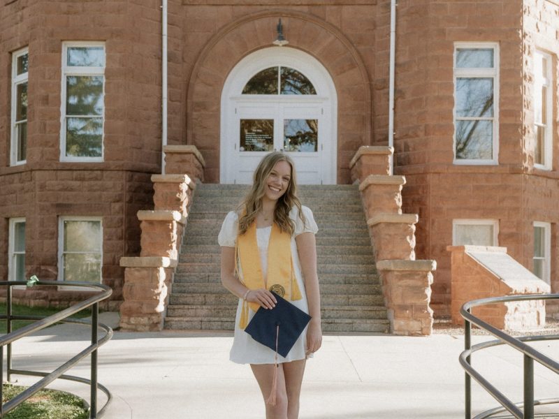 Claire Wahlberg holding her diploma, standing outside of the Flagstaff campus Old Main building.