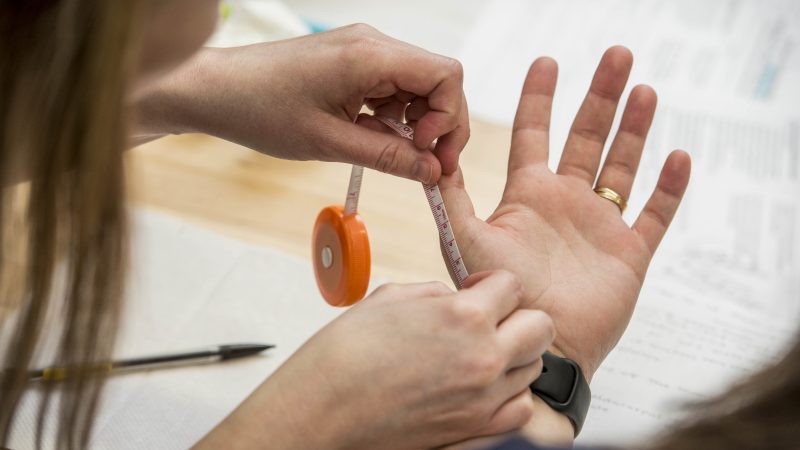 Person using a tape measure to measure the length of a persons thumb.