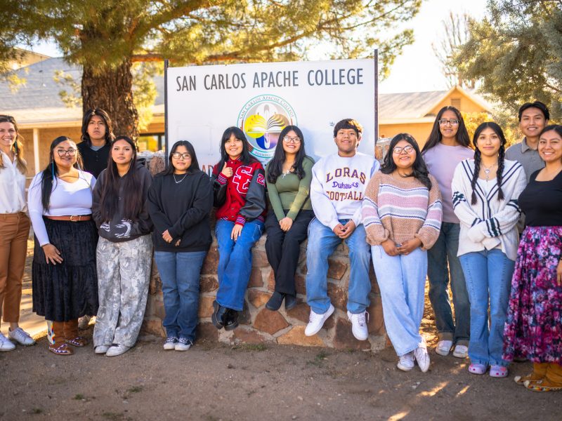 A group of students outside lined up in front of the San Carlos Apache College sign.
