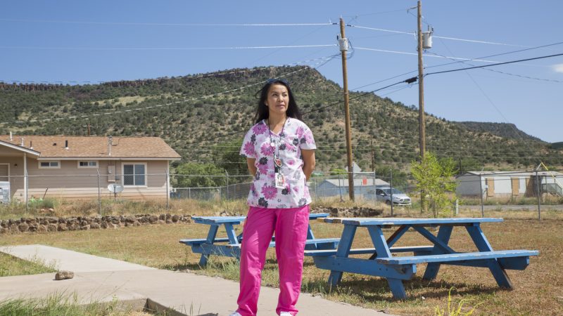 Community Health Representative standing in scrubs outside homes.