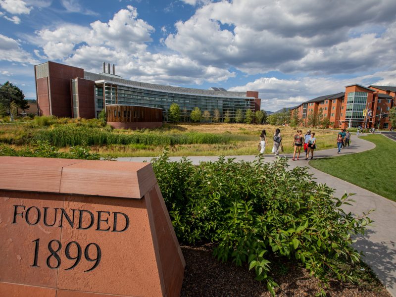Students walking next to N A U "Founded 1899" sign on campus.
