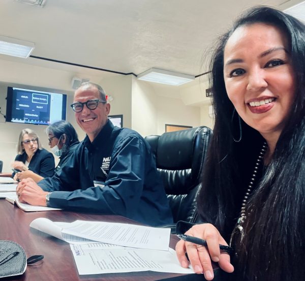 Four people seated at a table in a meeting room. The closest two are a woman taking the photo and a man sitting next to her, they are both smiling. The other two people are talking to each other.