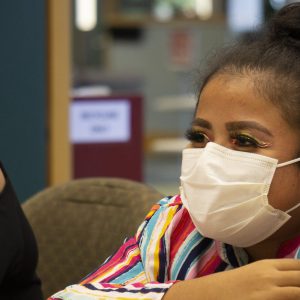 A masked student sits in a conference room during a coaching session. 