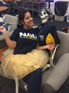 Giselle sitting in an armchair with a yellow tutu on, holding a skeleton decoration dressed in a polo