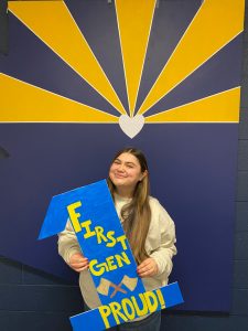 Leah Minero holding a cardboard "1" with the words "First-Gen Proud" painted on it