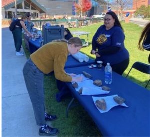 Student writing on a flyer on table outside