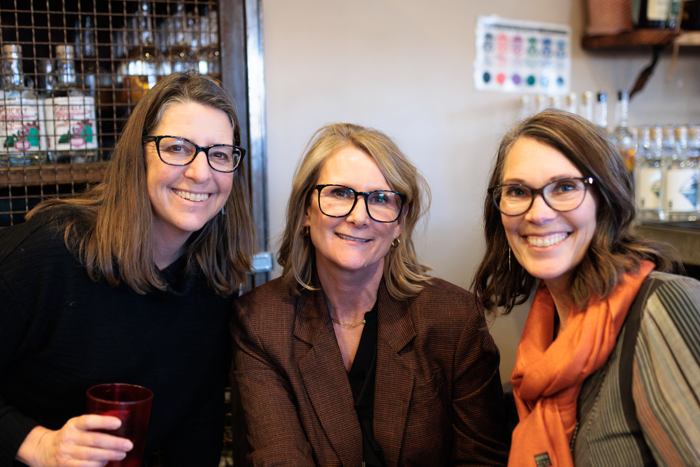 three women smiling in a public setting.