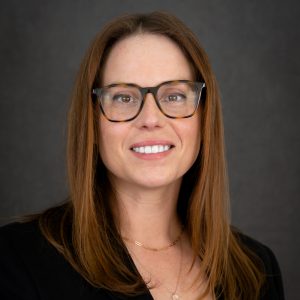 A headshot of Christine Kirby dressed in a black blazer with medium brown hair