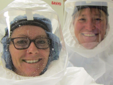 Bridget Barker poses with one of her students in a lab wearing white powered air purifying respirators.