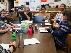 Heather Williamson is sitting at a long rectangular table with colleagues from a high school in Flagstaff. They are all smiling and laughing as she gestures and tells a story.
