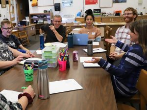 Heather Williamson is sitting at a long rectangular table with colleagues from a high school in Flagstaff. They are all smiling and laughing as she gestures and tells a story.