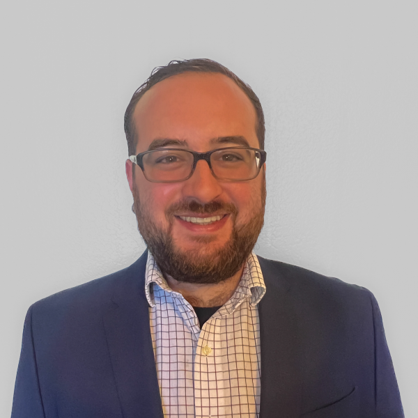 A photo of Jared Duval who has short brown hair, is wearing glasses and a blue suit jacket over a checked shirt.