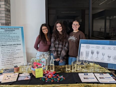 Daniela, Juliana, and Ayejah provide information about alcohol consumption at a community health fair. Visitors practiced pouring one drink to see what a single serving looks like. The students also talked about ways to cut back on alcohol consumption like pouring more mixers or using a smaller glass.