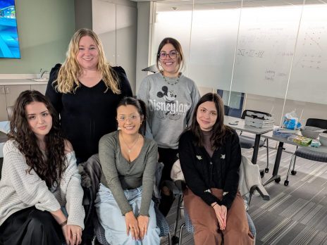 Tara and 4 students stand and sit together smiling