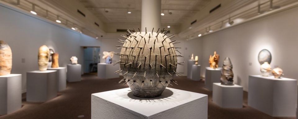 Spherical sculpture with spikes protruding in foreground, several large sculptures blurred in the background
