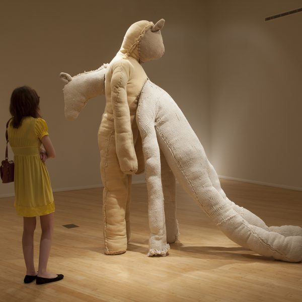 A woman looks upon large fabric statue of two converging animal figures
