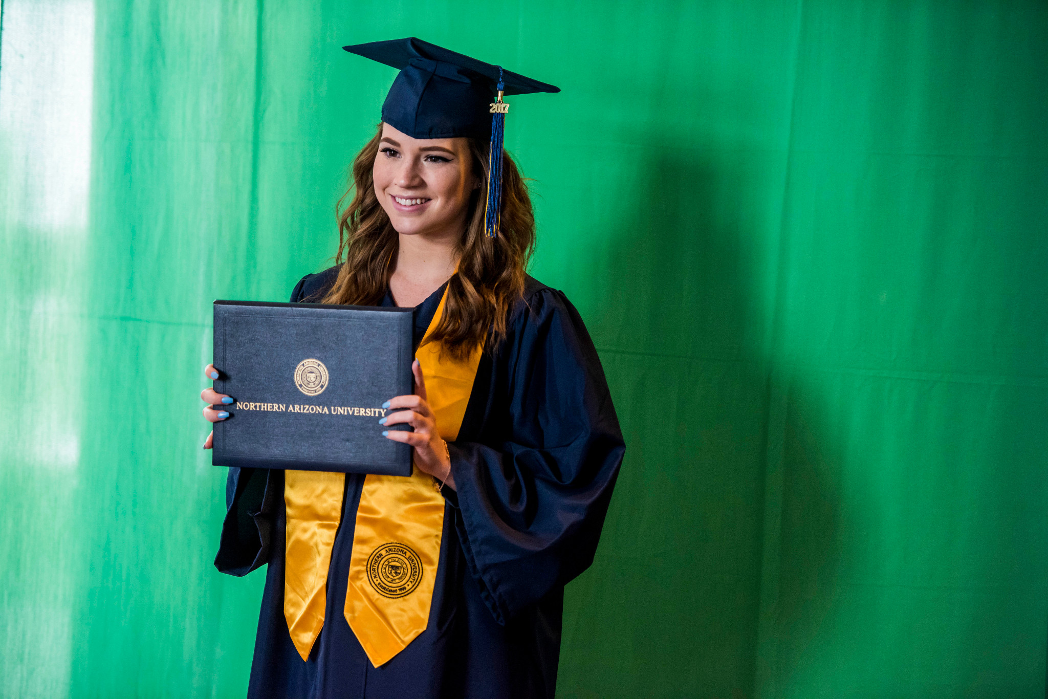 A student at N A U–Yuma holding up their diploma.