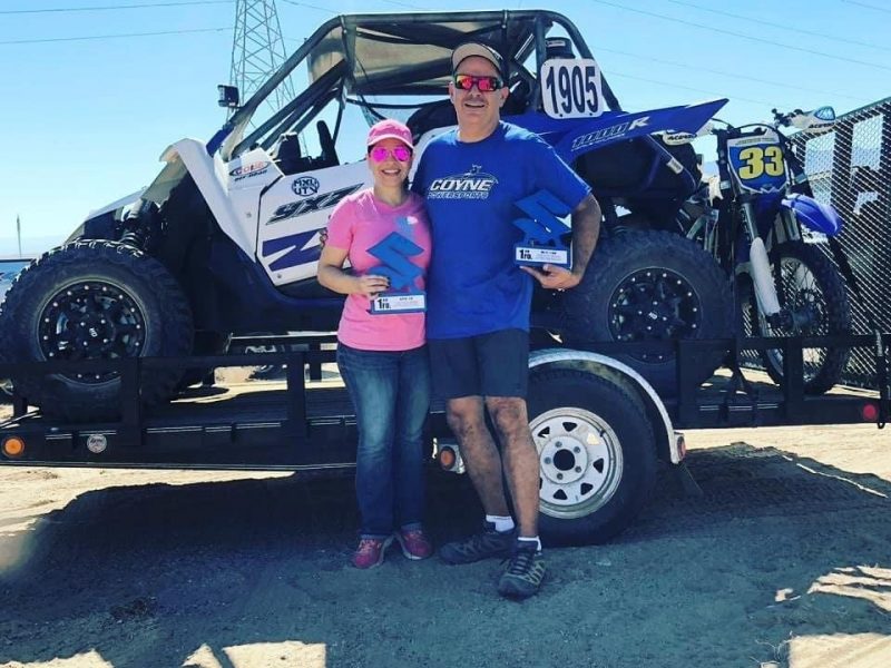 Dr. Monica Acosta Alvarado and parter holding trophies in front of an ATV and dirt bike.
